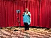 Donna Washington tells stories in front of an iPad and red curtain backdrop