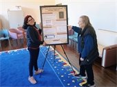 Two women pose with a research poster sitting on an easel 