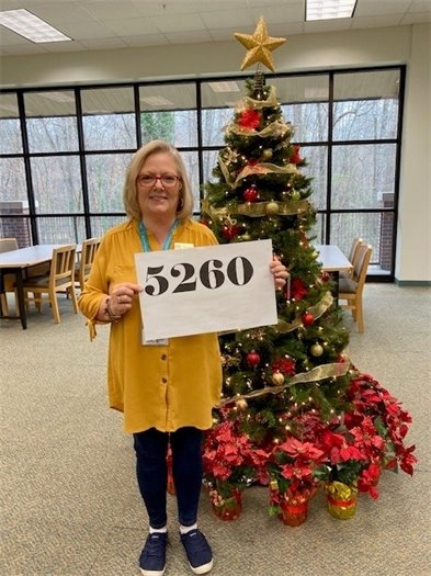 Tammie Foster poses in front of RPL South's Holiday Tree with a sign reading 5,260