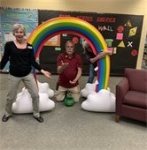 RPL staff pose with a giant inflatable rainbow decoration in the children's room