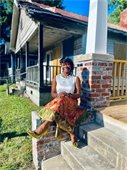 photo of Monica T. Davis sitting on the porch of a shotgun-style house