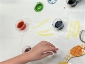 a child's hand works with paints and a wooden ornament to complete a sensory painting project