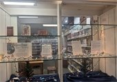 Library display with a "Cards for a Cause" theme, featuring festive greeting cards on glass shelves. Soft string lights and small decorative trees create a cozy, welcoming atmosphere.