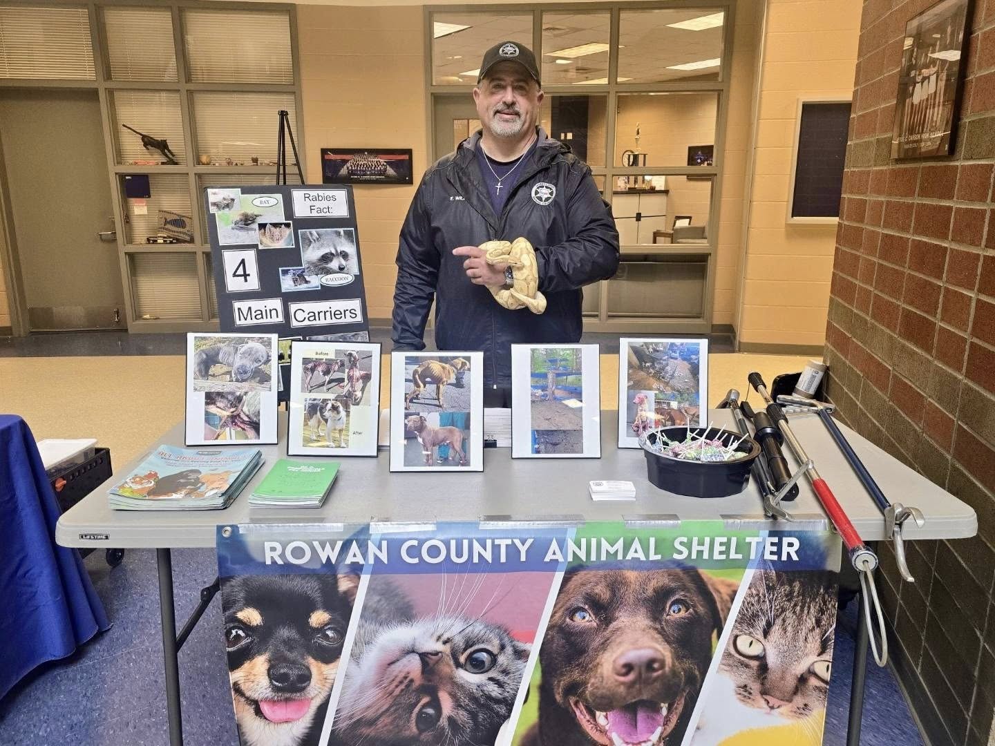 Man at Rowan County Animal Shelter booth holding a snake, with animal education boards and photos.