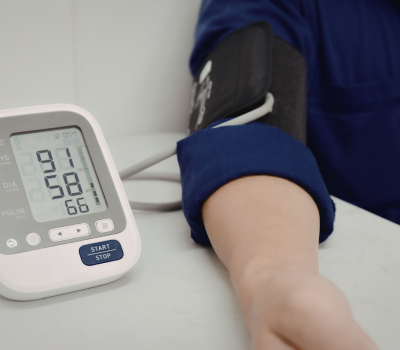 Arm in blue sleeve with cuff attached to a digital blood pressure monitor showing readings.