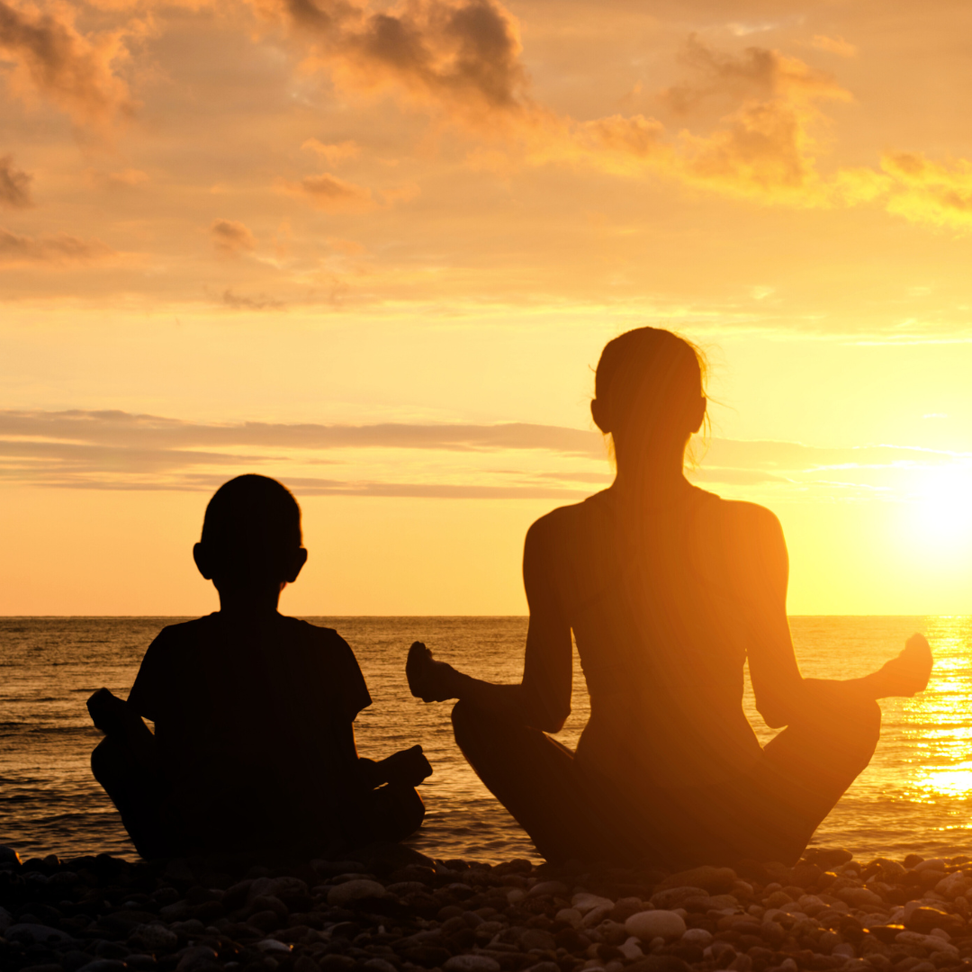 Silhouette of a girl and woman facing each other legs crossed with arms raised in a yoga pose.